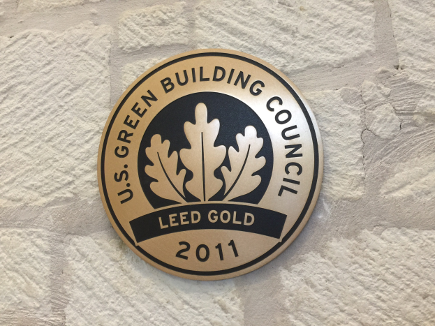 Logo der U.S. Green Building Council an einer Gebäudefassade, das ein grünes Schild mit weißer Umrandung, fetten schwarzen Text und einen umgebenden Lorbeerkranz zeigt.