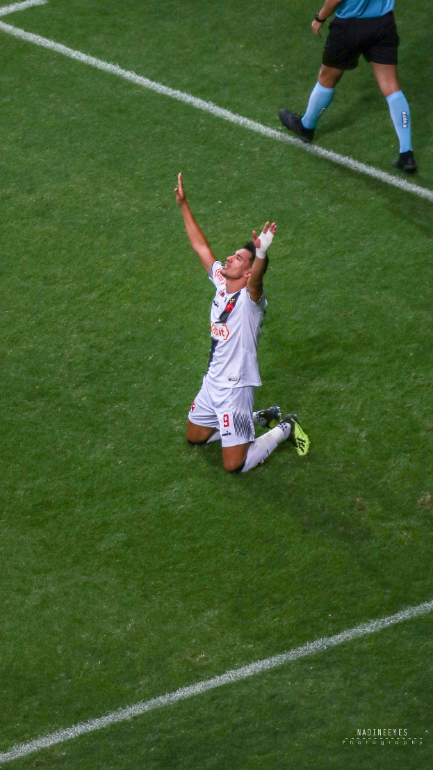 Ein Fußballspieler kniet auf dem Boden und streckt die Arme aus, während er ein Sportoutfit und -schuhe trägt.
